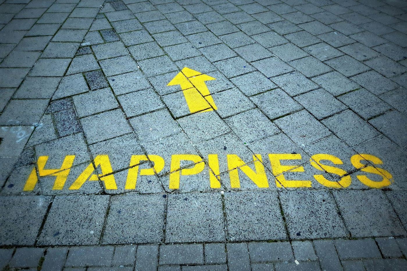 Gelber Pfeil mit dem Schriftzug „Happiness" auf Pflastersteinen — ein Hinweis Richtung Zuversicht